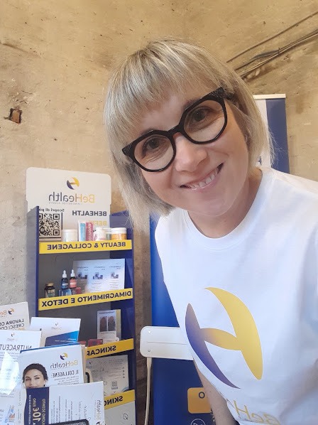 Smiling selfie in front of the Be Health stand shelf with Beauty & Collagene, Detox and Skincare labels